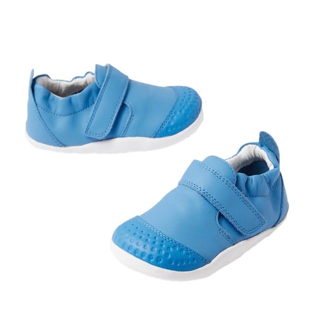 The Bobux Explorer Go First Walking Trainer in Azure Blue features soft leather, white soles, and Velcro straps, designed for babies learning to walk. Displayed against a plain white background.