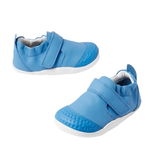 The Bobux Explorer Go First Walking Trainer in Azure Blue features soft leather, white soles, and Velcro straps, designed for babies learning to walk. Displayed against a plain white background.