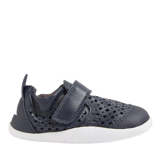 The Bobux Xplorer Go Punch Navy First Walker Sandal features perforated holes for breathability, a hook-and-loop strap, and a white rubber sole. Shown in side profile on a white background, these lightweight flexible baby shoes are perfect for little ones