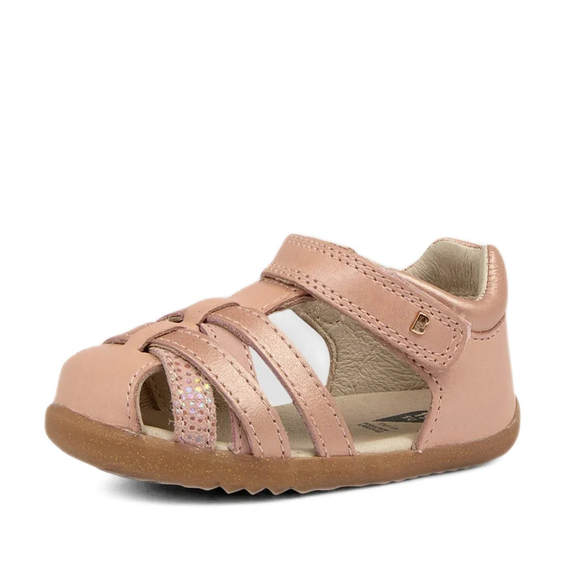The Bobux Step Ups Cross Jump Dusk Pearl Pink Closed Toe Sandal for first walkers features a closed toe, Velcro strap, cut-out sides, and a shimmery strap detail, shown on a white background.