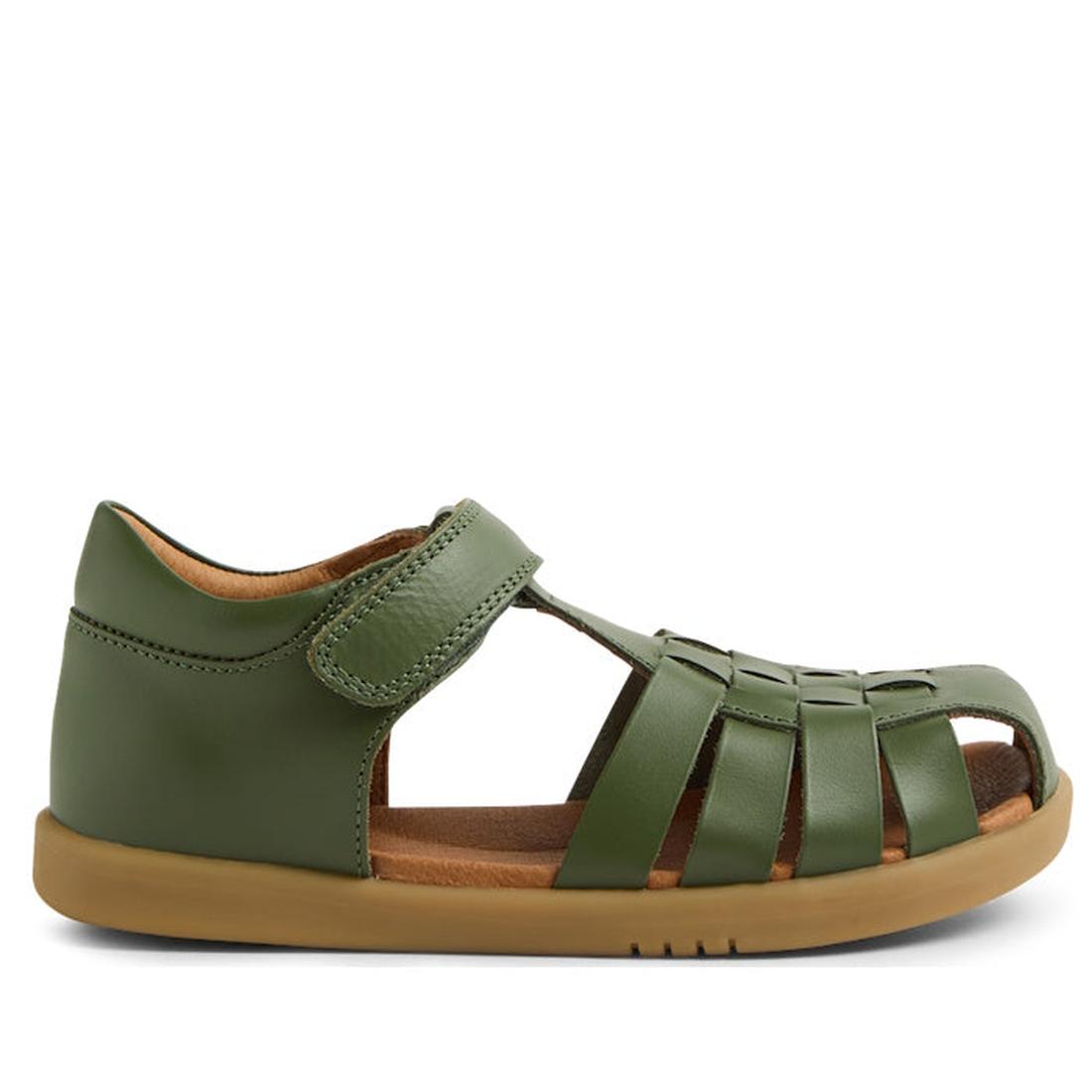 The Bobux Kid+ Plus Harbor Bronze Green Closed Sandal features woven leather straps, a brown sole, and a Velcro ankle closure. Shown in profile facing left, this water-friendly sandal is designed for kids and photographed against a white background.