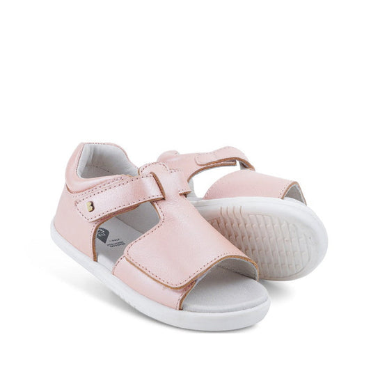 The Bobux IW Iwalk Mirror Seashell Pink 633414C girls’ open-toe sandals feature premium light pink leather, white soles, and an adjustable velcro strap, shown against a white background.