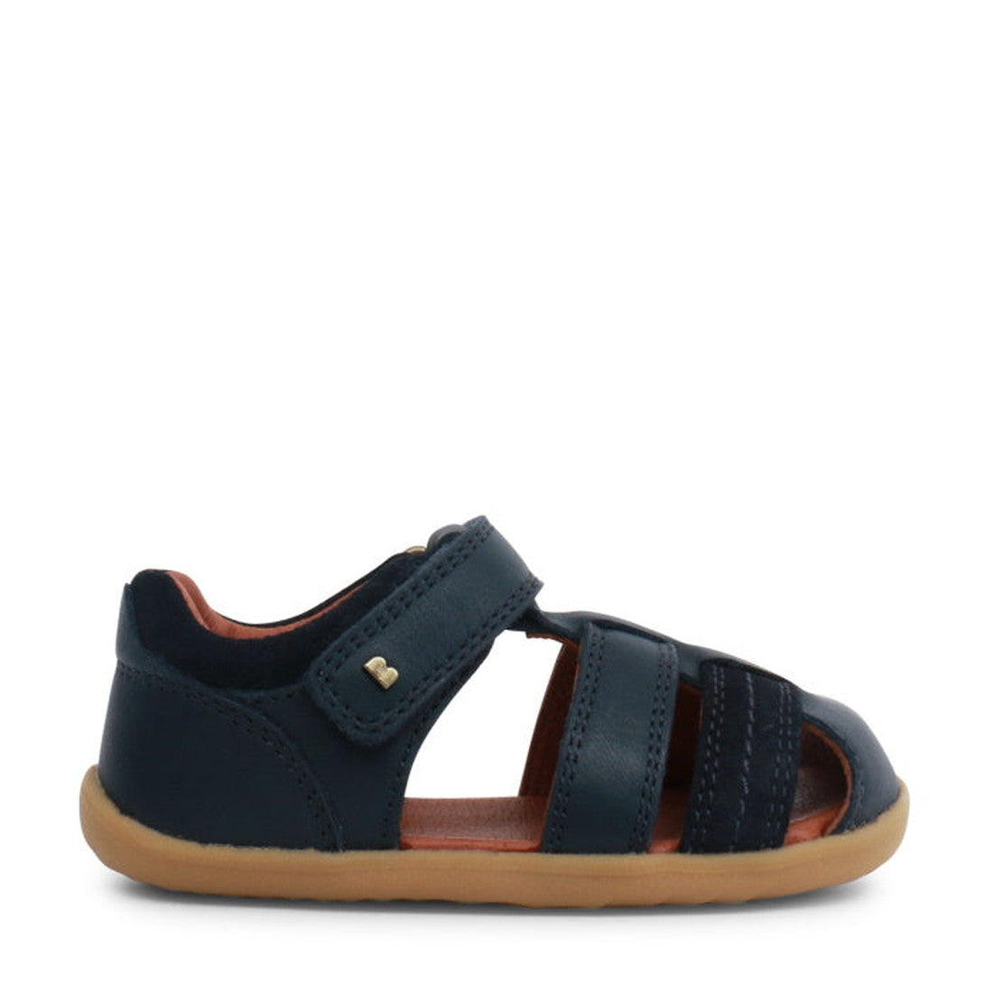 The Bobux Step Up Sandal Roam 729201A Navy Closed Toe is a toddler sandal with a leather upper, tan rubber sole, closed heel, open toe, and Velcro strap. Shown from the side on a white background. Ideal as first walking sandals for little ones., 942005733