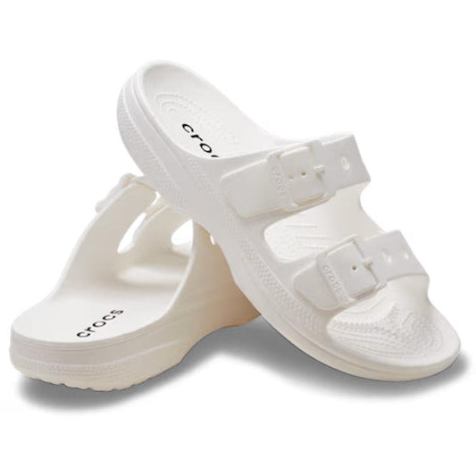The Crocs Womens Classic Saturday Sandal Slide in white features two adjustable buckle straps on each shoe for a personalized fit—one sandal stands upright, while the other leans against it.