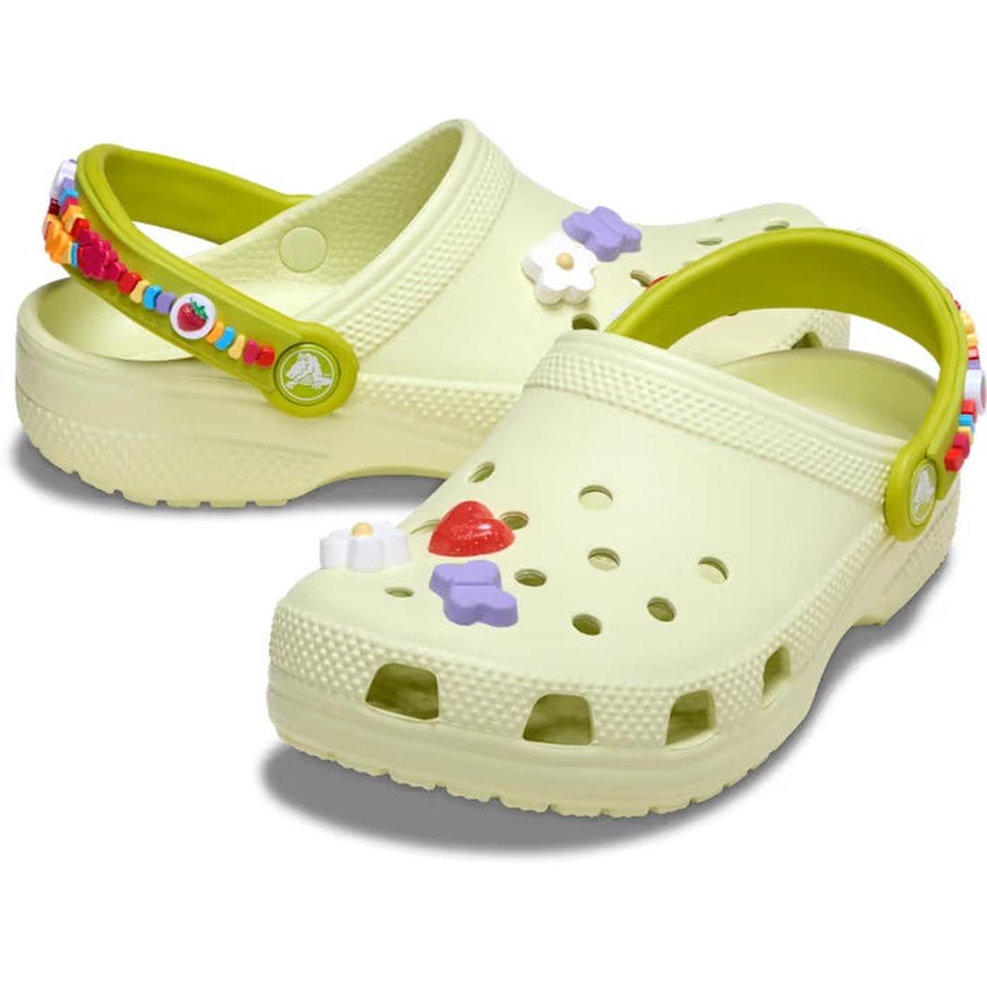 A pair of frothy green Crocs Classic Clogs for kids with friendship bracelet embellishment on the heel strap and Jibbitz charms.