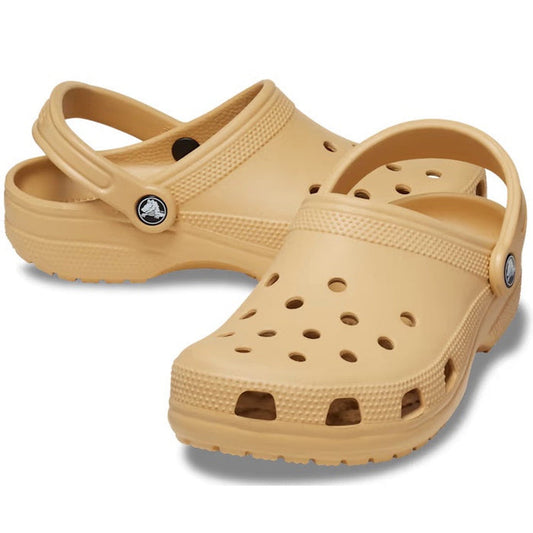 The Crocs - Classic Clog Wheat Tan Adults are beige unisex clogs featuring ventilation holes and adjustable heel straps for lightweight comfort, displayed on a white background.