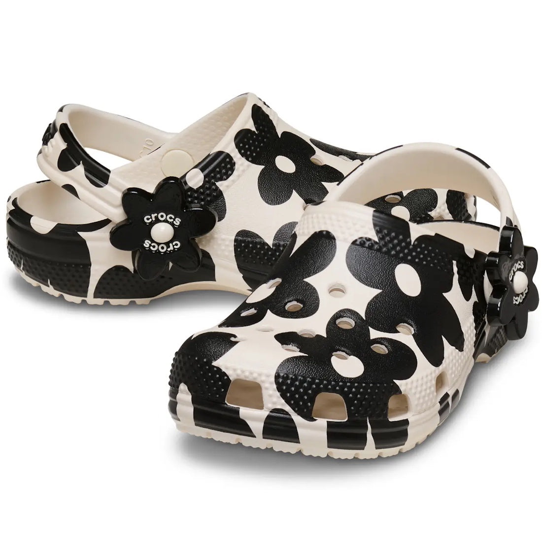 A pair of Crocs Kids Toddlers Classic Clog K Pop Petals Off White Black, showcasing a bold black and white floral print and flower-shaped Crocs logo charms on the straps, delivering signature Crocs Comfort with every step.