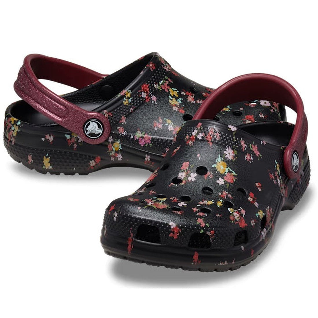 The Crocs Kids Youths Classic Clog K Ditsy Floral Black Multi Sandal, featuring ditsy floral graphics and maroon straps, is displayed against a white background.