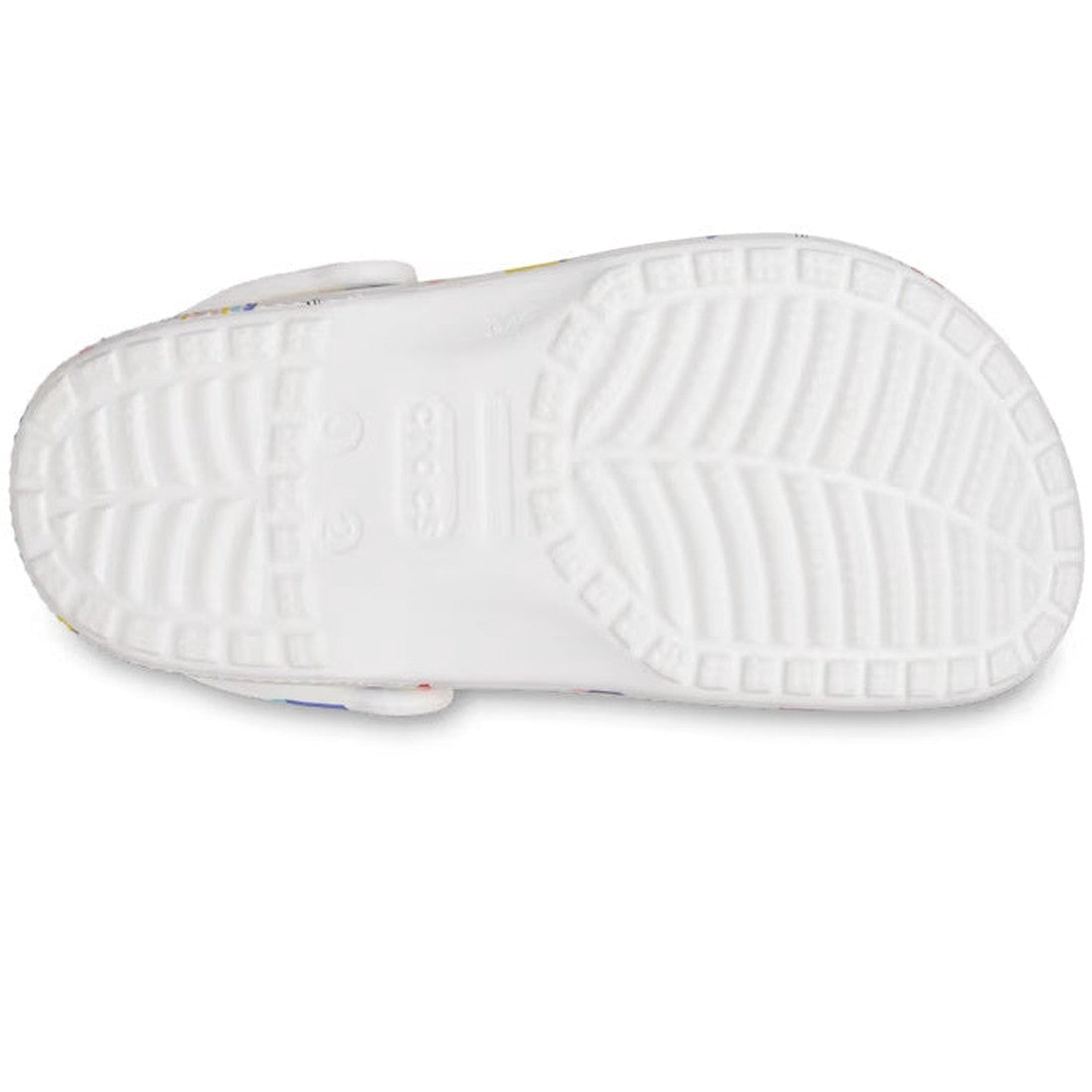 The image shows the bottom view of the Crocs Kids - Youths Classic Clog K Doodle Print White Multi Sandal, featuring a white textured rubber sole with straight and zigzag grooves for traction. The Crocs brand name is embossed at the center., 196265775811,
