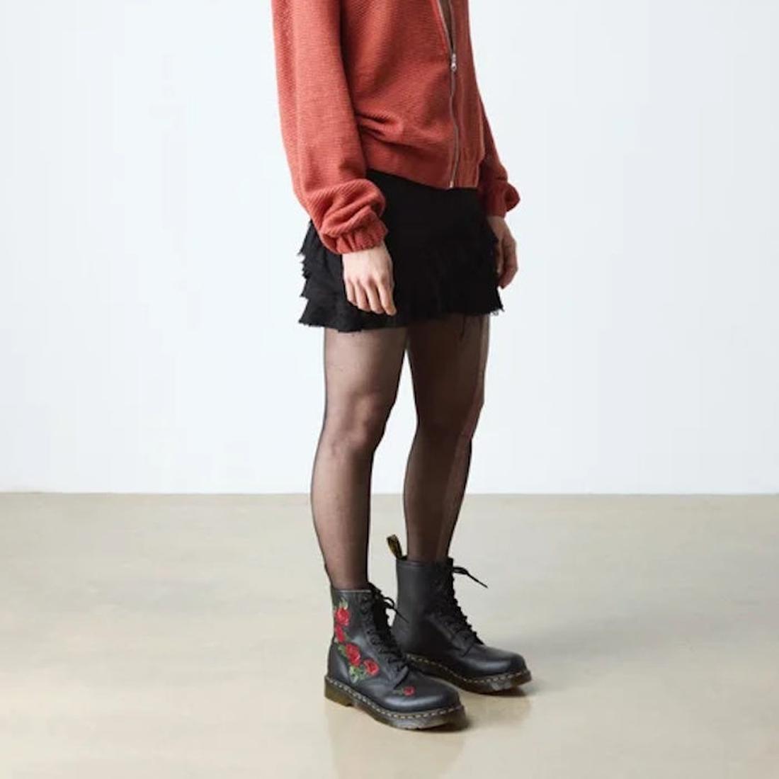 Person wearing a rust zip-up jacket, black mini skirt, sheer black tights, and Dr Martens 1460 Vonda Red Roses Softy T Leather Boots, standing indoors on a light floor against a plain background., 190665206036, 190665206043, 190665206050, 190665206074, 19