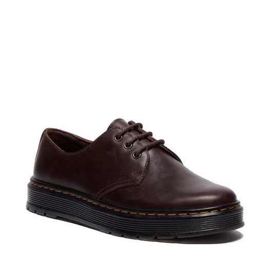 The Dr Martens Brookline Lo Dark Brown Crazy Horse Leather Shoe features a 3-eye design, black laces, metal eyelets, and a thick black rubber sole with signature yellow stitching around the edge.