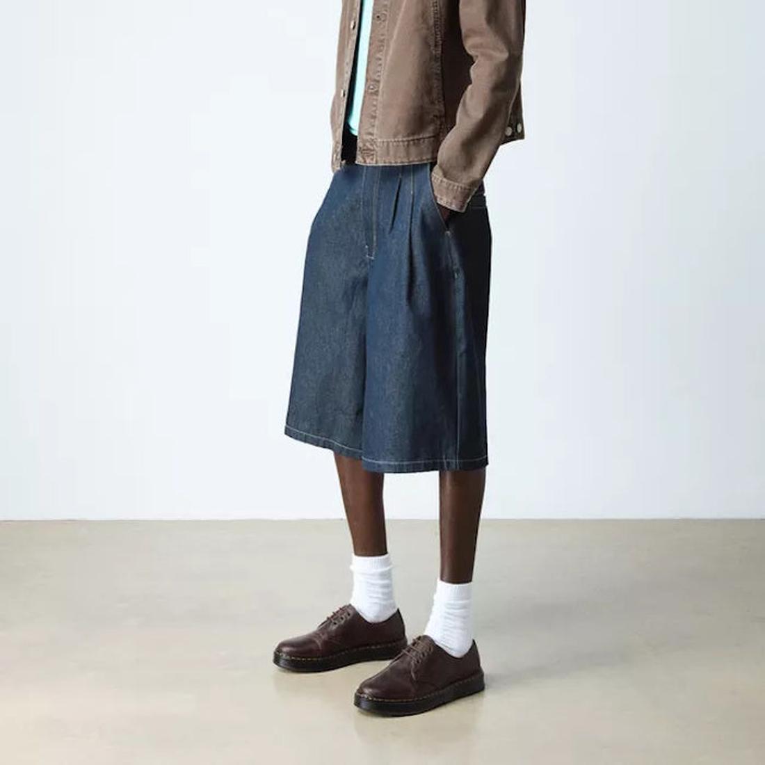 A person in a brown jacket, light green shirt, knee-length wide denim shorts, white socks, and Dr Martens Brookline Lo Dark Brown Crazy Horse Leather Shoe with SoftWair insole stands on a light floor against a plain background. Face not visible., 52062, 5