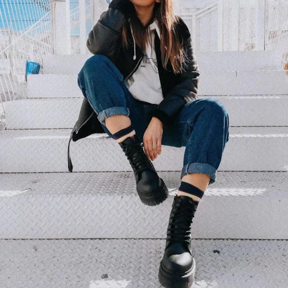 A person sits on white metal stairs outdoors, wearing rolled-up blue jeans, a gray hoodie, a black jacket, and Dr Martens Jadon II Black Mono Vegan 8 Up w/Zip boots. Their face is partially out of frame, with one knee raised for a casual vibe., 47978, 190