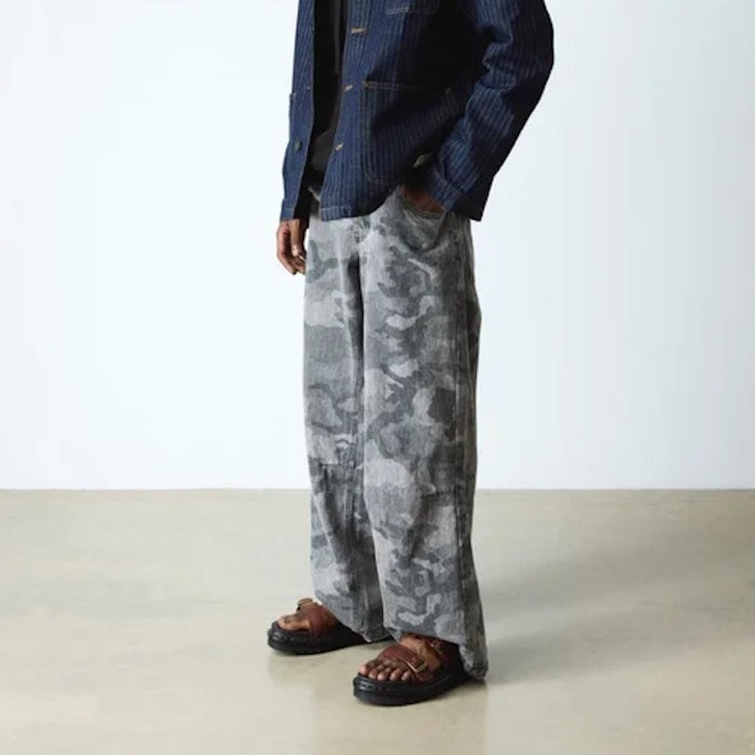 A person stands indoors in loose gray camo pants, a dark blue striped jacket, and Dr Martens Myles Cashew Ambassador Brown Leather Sandals. The image is cropped at the shoulders against a plain, light background., 49260, 190665772081, 190665772098, 190665