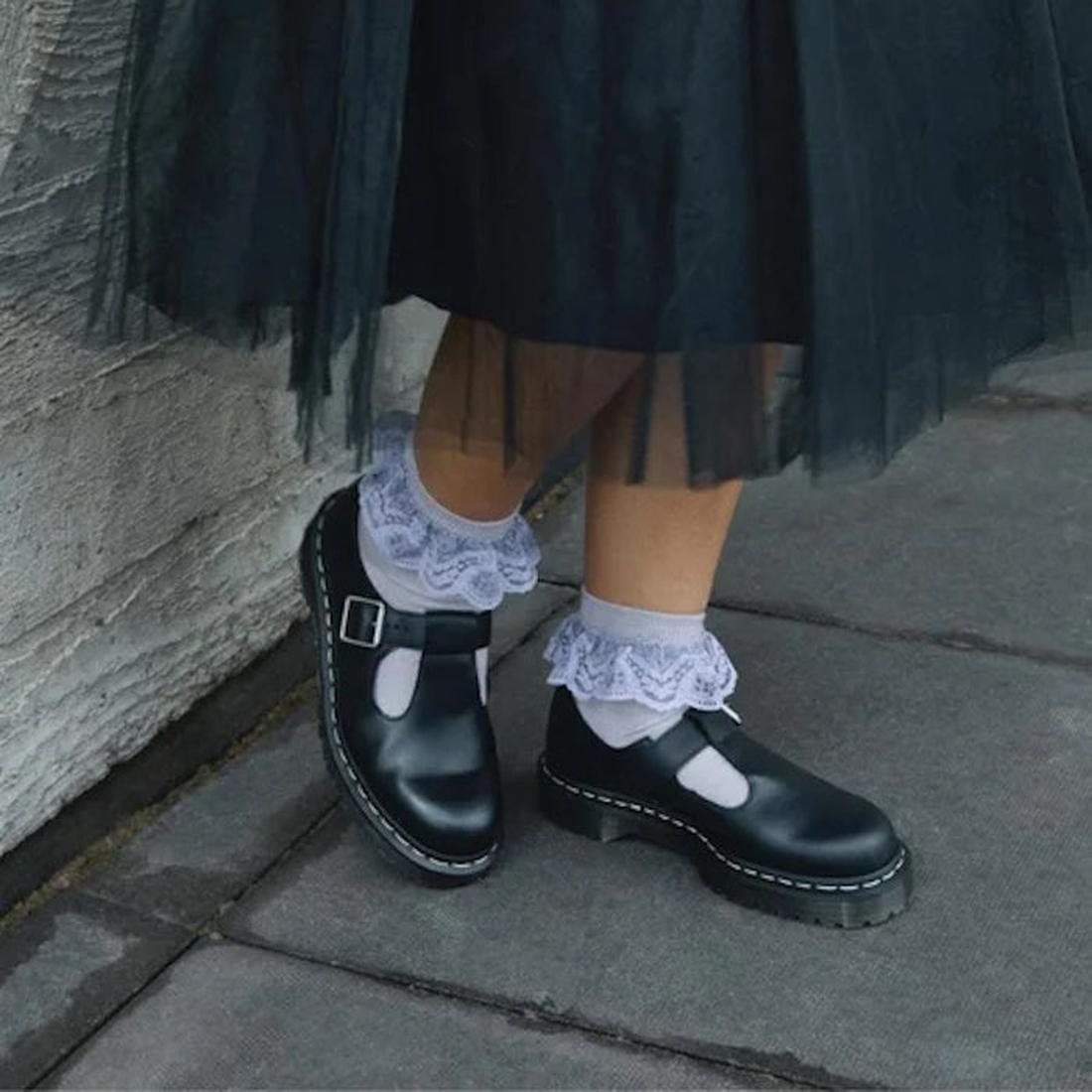 Black Polley Dr Martens T Bar Shoes shoes with white  socks and lace ruffles against a stone wall.,
190665696905,
190665696912,
190665696936,, 45112, 45113, 190665696905, 190665696912, 190665696936, 45118, 45119