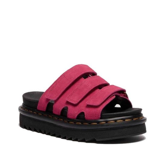 The Dr Martens Raine Fuchsia Pink Greasy Suede Leather Slides feature thick black EVA Zebrilus soles and three wide, bright pink suede straps with adjustable Velcro closures.