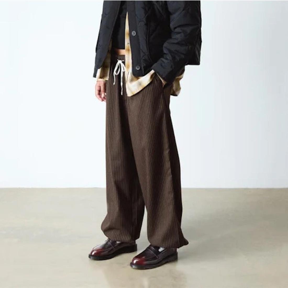 A person stands indoors with hands in pockets, wearing loose brown pinstriped pants, a beige shirt, a black jacket, and Dr Martens Temara Cherry Red Arcadia Leather Loafers. Their face is not visible., 190665747560, 190665747577, 190665747591, 52060, 5206