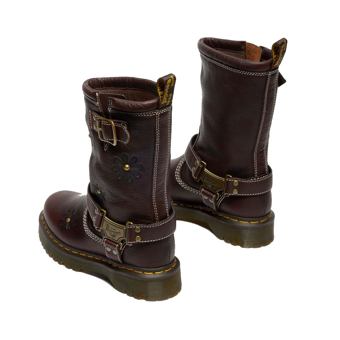 The Dr Martens Anistone Hi Flower Bex Grizzly Dark Brown boots feature floral detailing, decorative buckles, yellow stitching, thick soles, and rear pull tabs. These biker-inspired leather mid-calf boots are shown from an angled rear view.