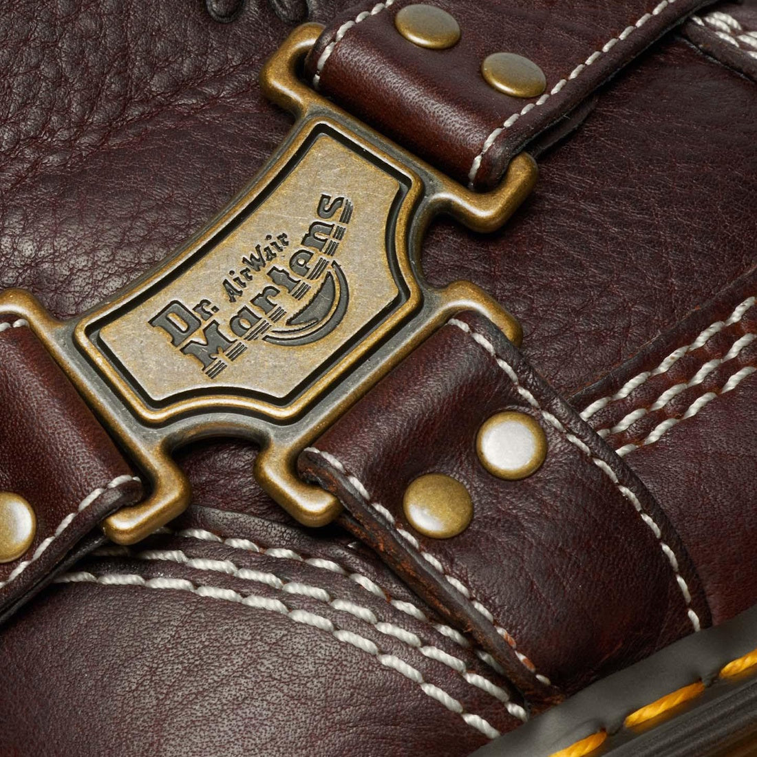 Close-up of the Dr Martens Anistone Hi Flower Bex Grizzly Dark Brown showing detailed white stitching, brass rivets, and a metal Dr. Martens logo plate on the brown leather strap.