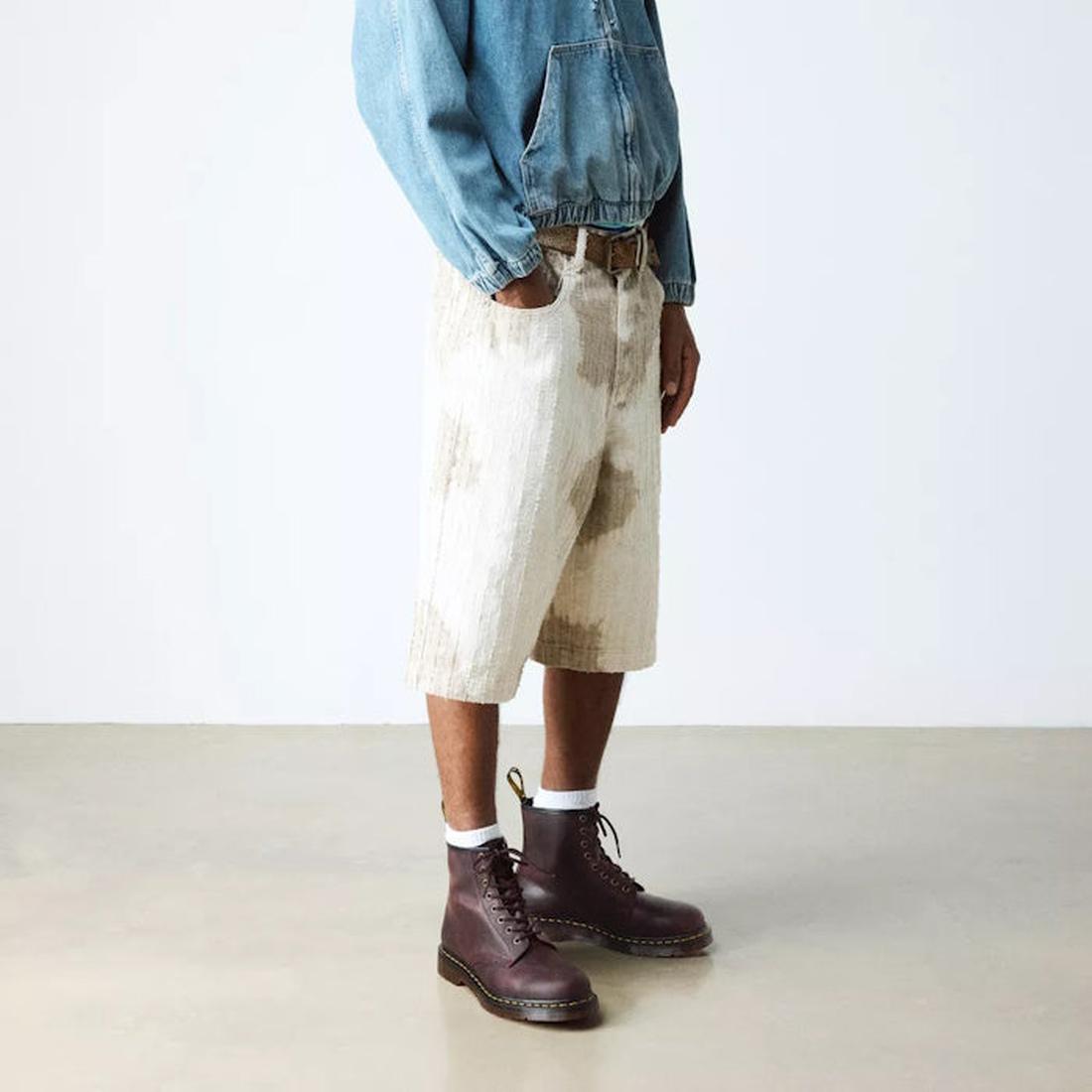 A person stands indoors against a plain background, wearing a blue denim jacket, light-colored stained knee-length shorts, white socks, and Dr Martens 1460 Cherry Red Crazy Horse Waxy Leather 8 Eye Boots., 190665786835, 190665786842, 190665786859, 1906657
