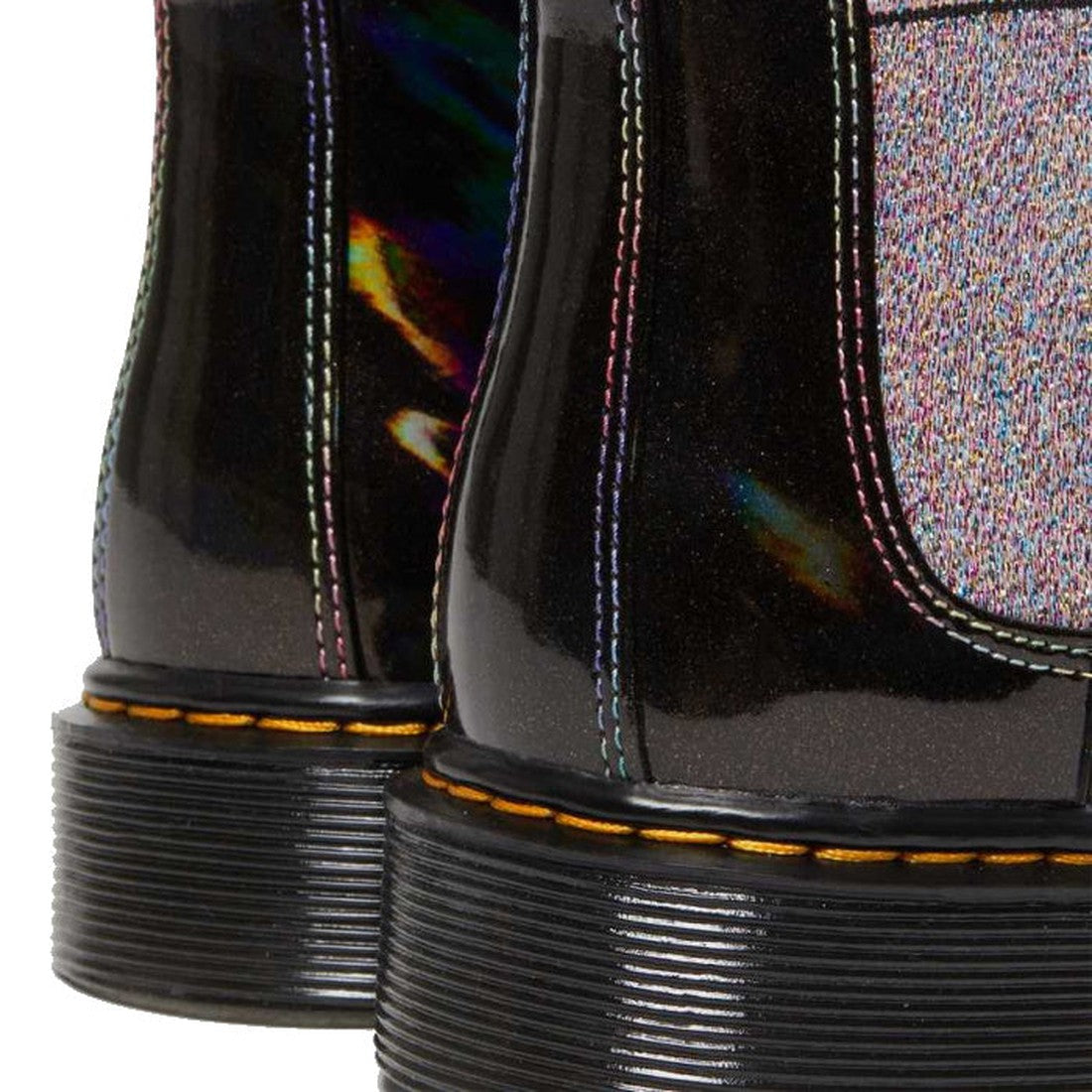 Close-up of Dr Martens Kids Juniors 2976 J Chelsea Boot Black Lightshow Sparkle Rays, featuring a glittery rainbow finish, rainbow-colored stitching, and thick black soles with visible yellow stitching., 190665495171, 190665495195, 190665495218, 190665495