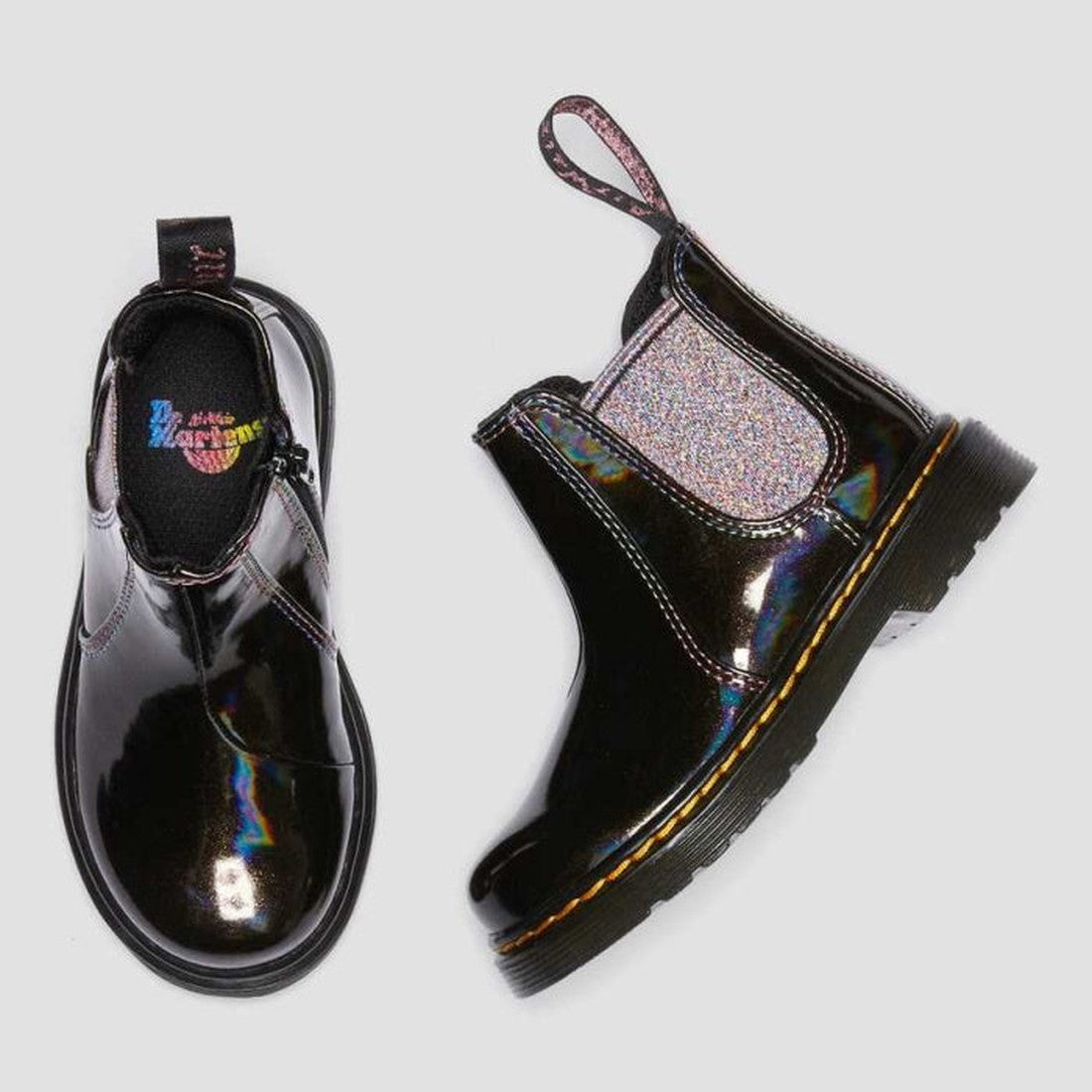 Two Dr Martens Kids Toddlers 2976 T Chelsea Boot Black Lightshow Sparkle Rays (UK8) shown: one upright, one on its side. Features shiny black iridescent material, glitter side gussets, and yellow stitching on a light gray background., 190665494914, 190665