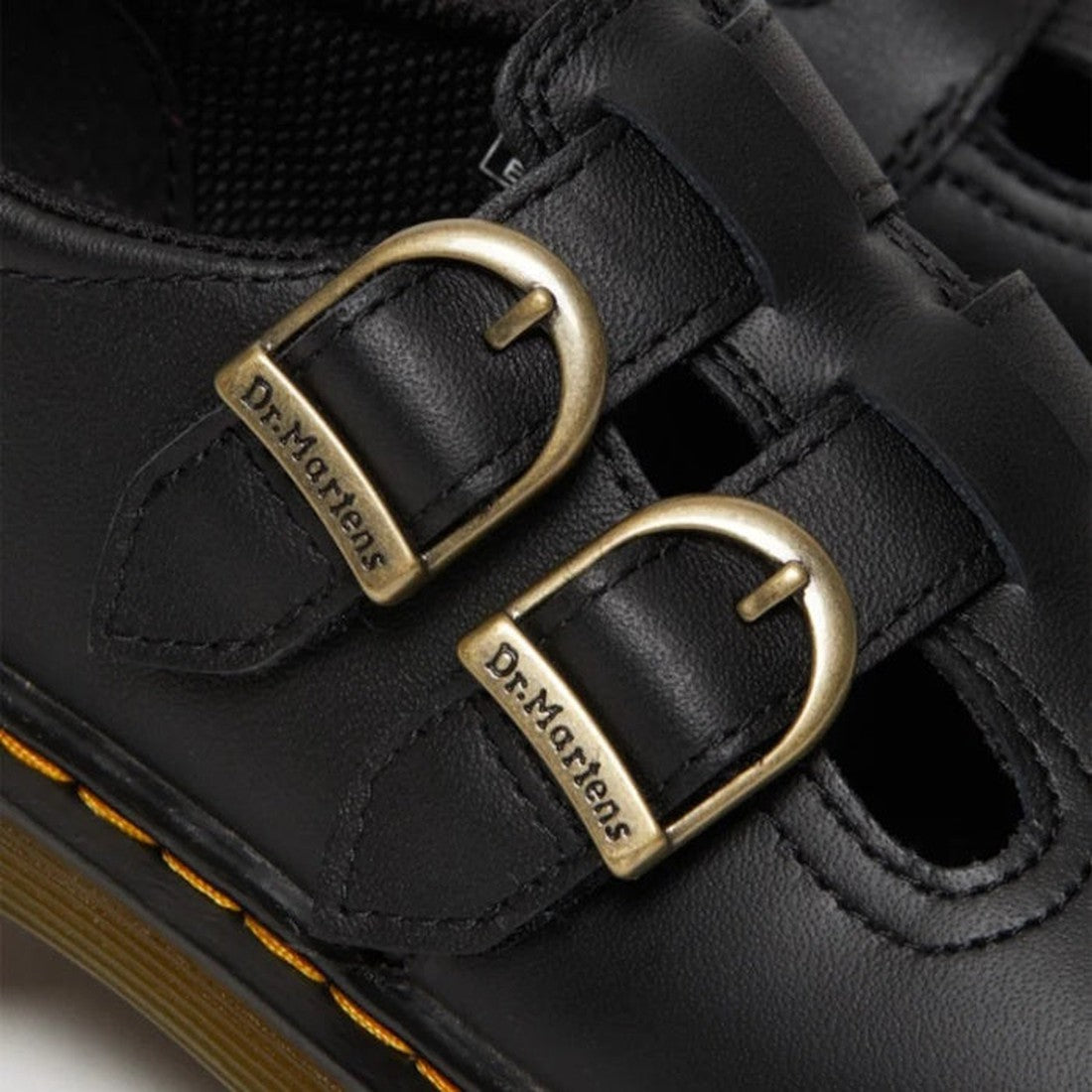 Close-up of black Dr. Martens Kids 8065 J Softy T Mary Jane leather shoes featuring two brass buckles with engraved logos, visible stitching, signature yellow welt stitching, and air-cushioned soles., 41982, 41983, 190665537093, 190665537109, 190665537000