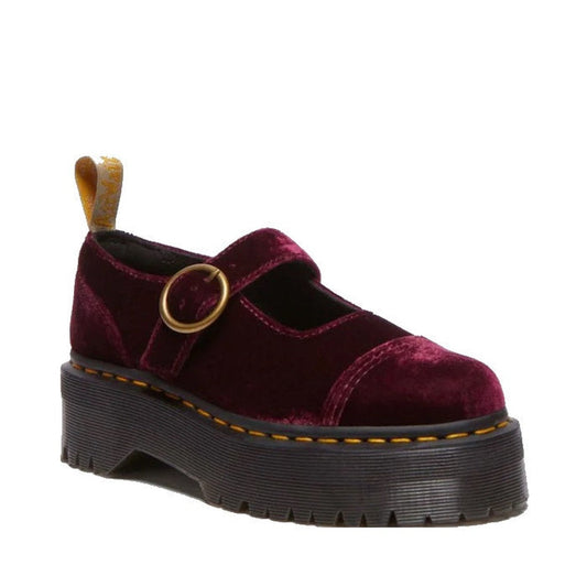 The Dr Martens Addina Vegan Cherry Red Velvet Mary Jane Quad Platform features a chunky quad sole, Goodyear-welted construction, visible yellow stitching, gold buckle strap, and a yellow heel loop in vegan velvet.
