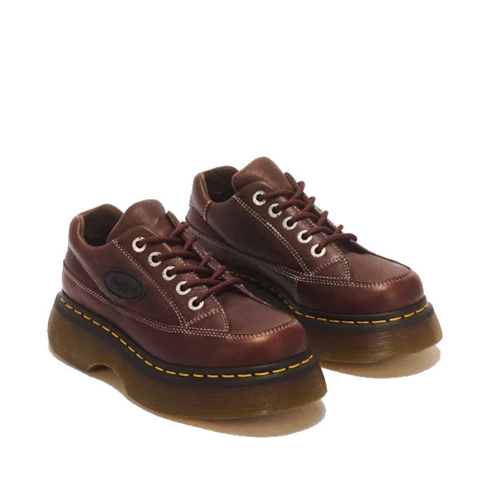 A pair of Dr Martens Buzz 5i Dark Brown Grizzly Leather Shoes with white stitching, thick translucent brown chunky barrel-edge Buzz soles, and yellow stitching around the welt, viewed from an angle.
