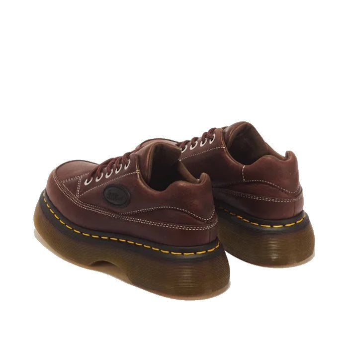 Dr Martens Buzz 5i Dark Brown Grizzly Leather Shoes feature thick, dark translucent chunky barrel-edge soles, yellow stitching, and white accent stitching on the uppers. Shown from a rear side angle against a white background, these platform shoes boast b
