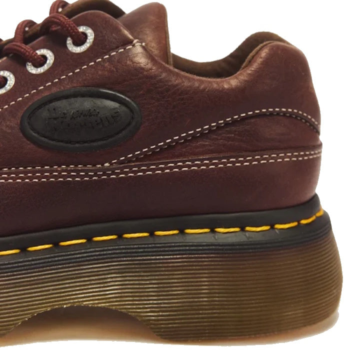 Close-up of the Dr Martens Buzz 5i Dark Brown Grizzly Leather Shoe, featuring visible stitching, a thick tan translucent chunky barrel-edge Buzz sole with a black rubber edge, and signature yellow stitching above the sole—evoking bold ’90s silhouettes.