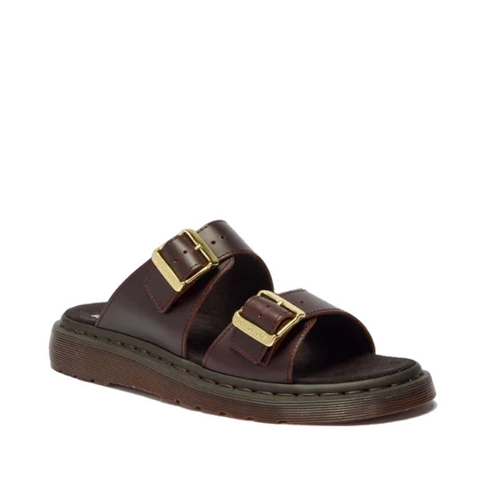 The Dr Martens Josef Charro Atlas Slide Sandal features brown leather, two adjustable gold buckles, Goodyear-welted construction, a thick ridged sole, and visible edge stitching.