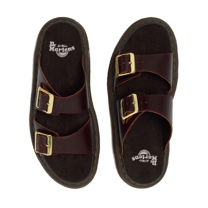 A pair of Dr Martens Josef Charro Atlas Slide Sandal Leather in dark brown with two gold-buckle straps, Goodyear-welted soles, and visible footbed logo, displayed on a white background.