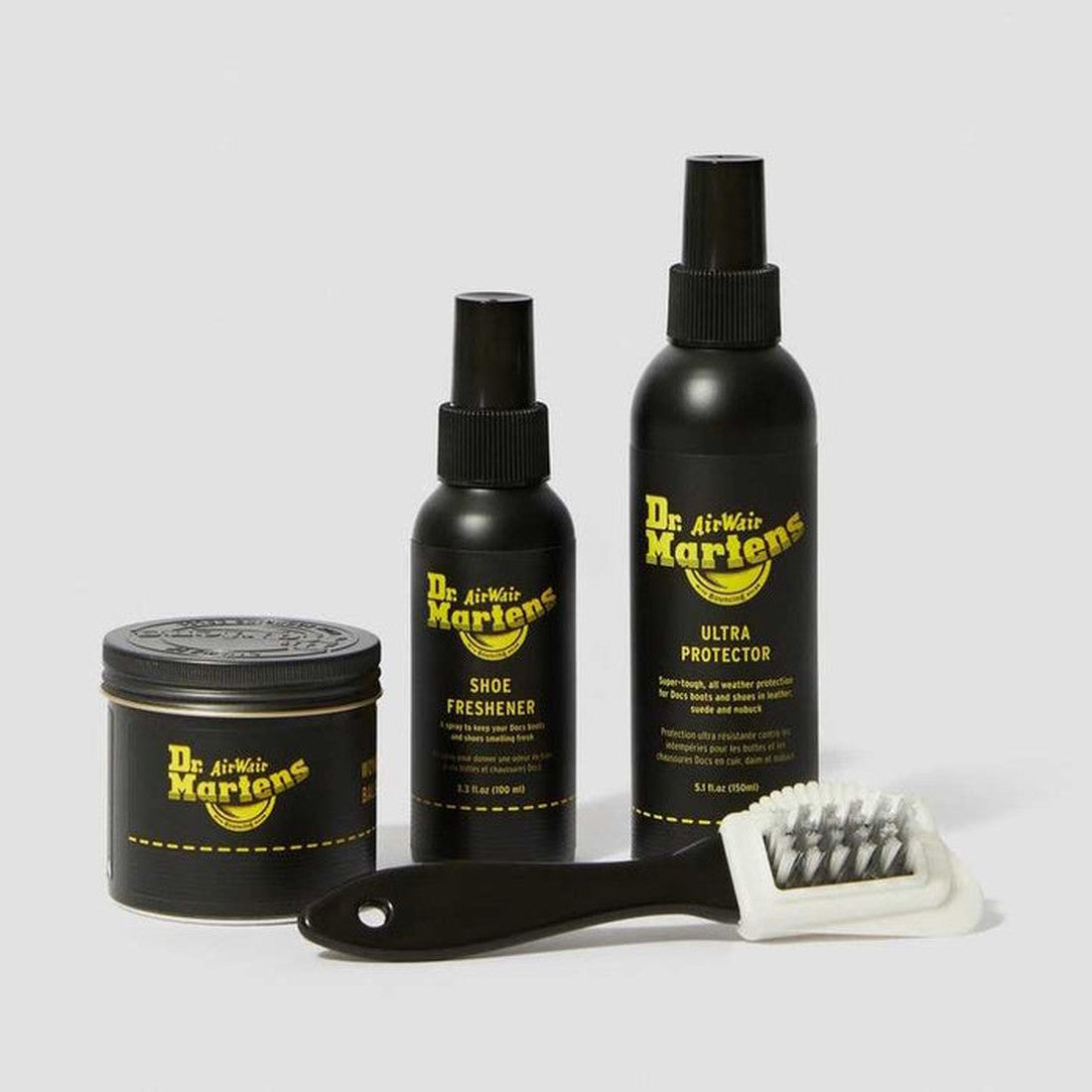 The Dr Martens Shoe Care Kit Ultimate Box includes Wonder Balsam, shoe polish, Ultra Protector spray, shoe freshener, and a black brush with white bristles—all neatly displayed on a light gray background., 190665251326