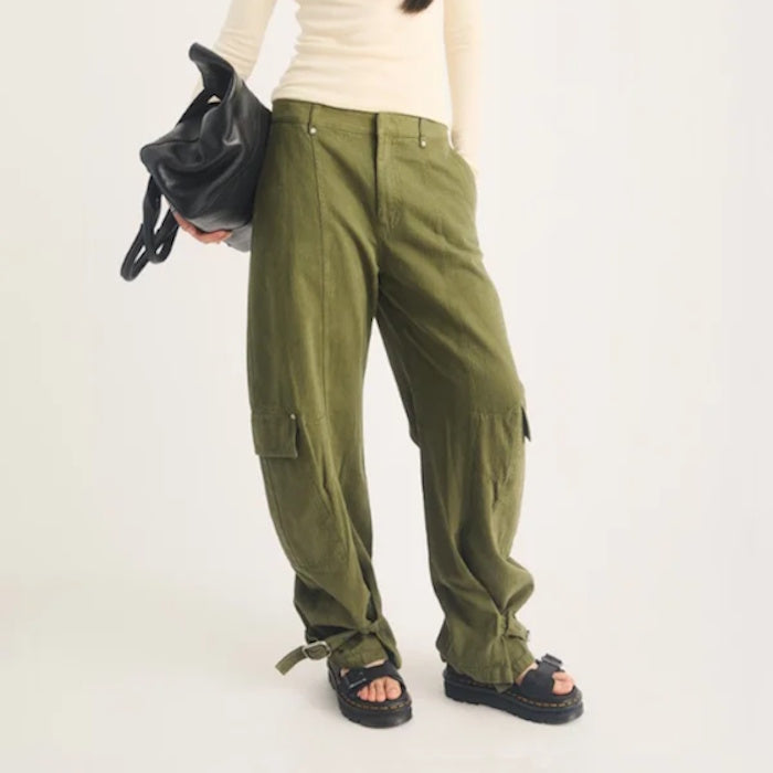 A person wearing olive green cargo pants and black Dr Martens Zebzag Black Pisa Leather 3 Strap Sandal, carrying a black handbag.