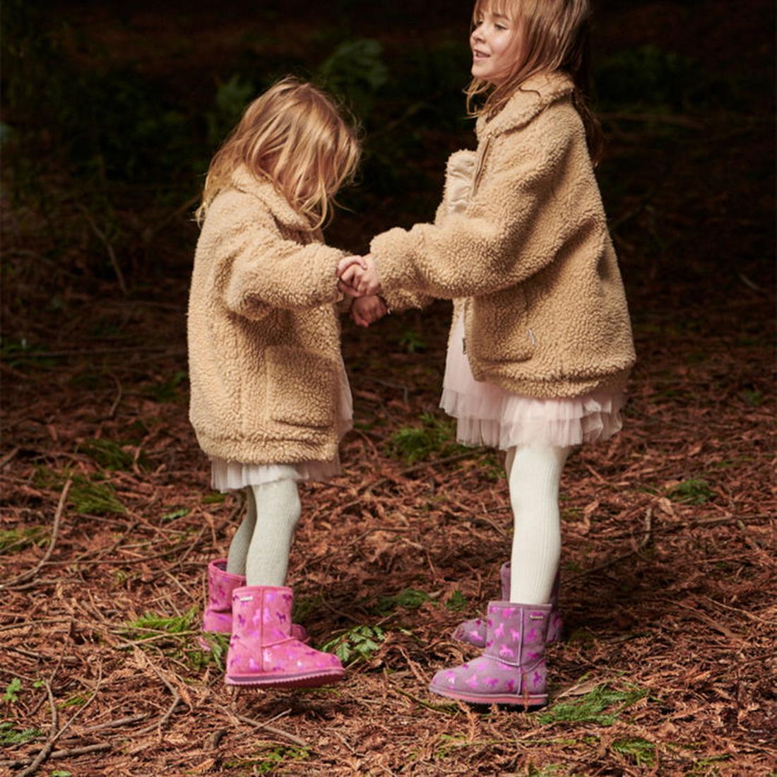 Two girls hold hands in the woods, wearing pink EMU NZ Brumby Unicorn Lo boots—waterproof wool with sturdy soles and easy pull-on style.  ksnz