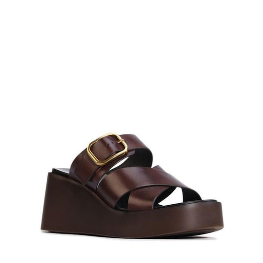 The EOS Aris Womens Chestnut Brown Leather Wedge Slide features wide crisscross premium calf leather straps, a large gold buckle, a chunky wedge sole, anatomical footbed, open toe design, and easy slip-on style.