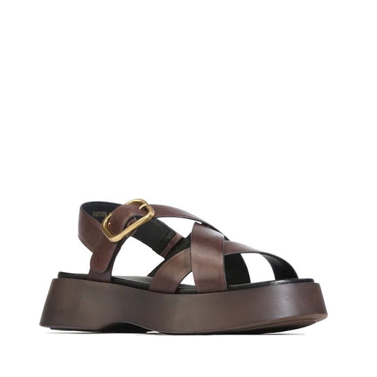 The EOS Barista Chestnut Leather Platform Sandal is a women’s shoe featuring wide crisscross straps, a statement gold buckle, and an open toe in brown leather, shown from the side against a white background.