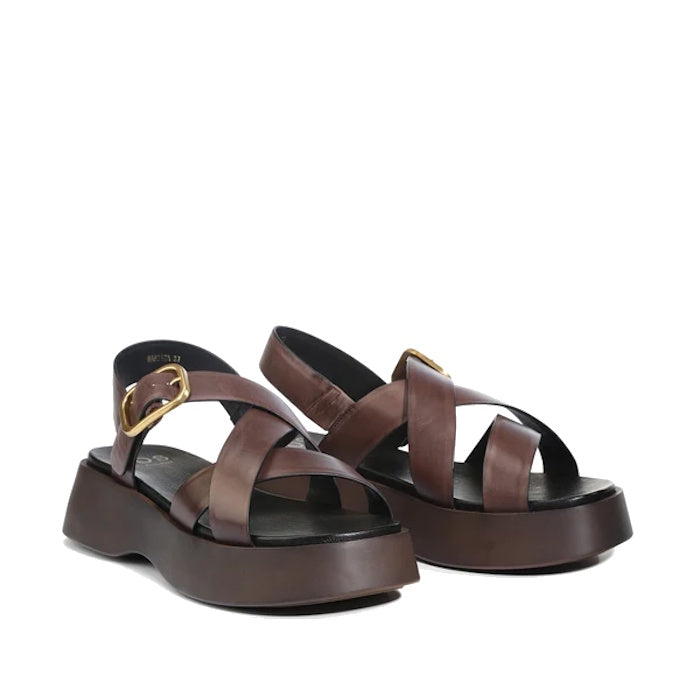 Introducing the EOS Barista Chestnut Leather Platform Sandal: a chic pair of chestnut brown women’s sandals crafted with crisscross leather straps, accented by a statement gold-tone buckle and grounded on bold black soles. Featuring a slightly elevated ch