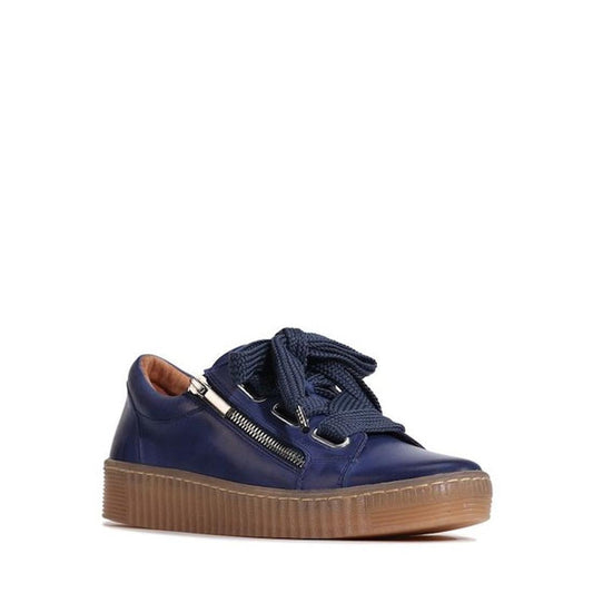 The EOS Jovi Dusk Blue Leather Women's Trainer features a side zip, thick matching laces, a brown textured rubber sole, and a sleek design, shown against a plain white background.