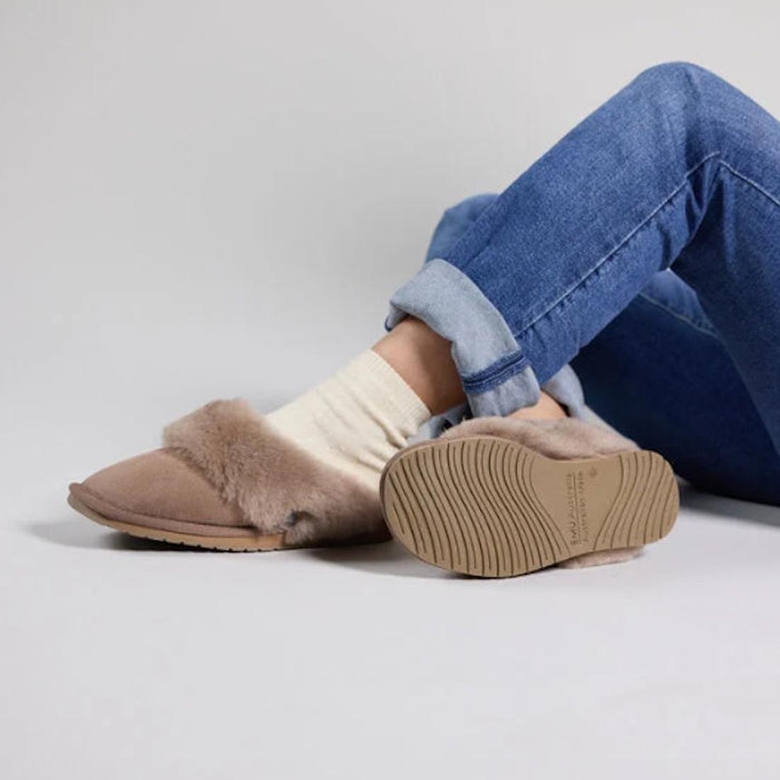 A person in rolled-up blue jeans, cream socks, and Emu Womens Eden Mushroom Platinum Sheepskin Scuff Slippers sits cross-legged on the floor, displaying the cozy slipper’s sole and top against a plain background., 9330071337912, 9330071337929, 93300713379