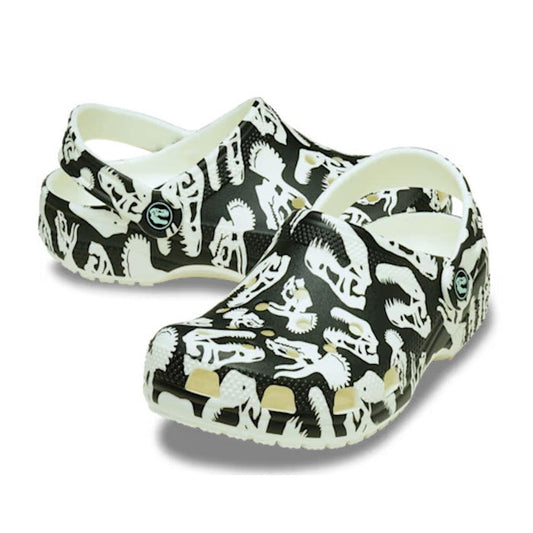 The Crocs Kids - Youths Classic Glow Dino Clog K Black Sandal features a white base with black dinosaur skeleton graphics and adjustable heel straps—perfect for adventurous little explorers!.
