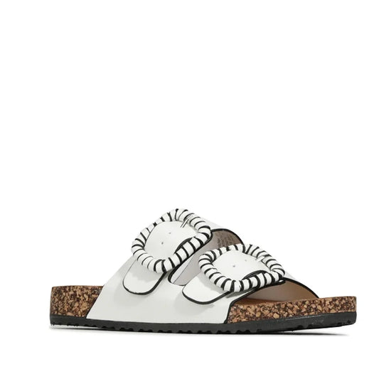 The Los Cabos Jirona White Women’s Double Strap Slides are shown from a side angle on a white background, featuring two wide buckled straps with black-and-white trim, an anatomically shaped footbed, a cork sole, and a black rubber bottom.