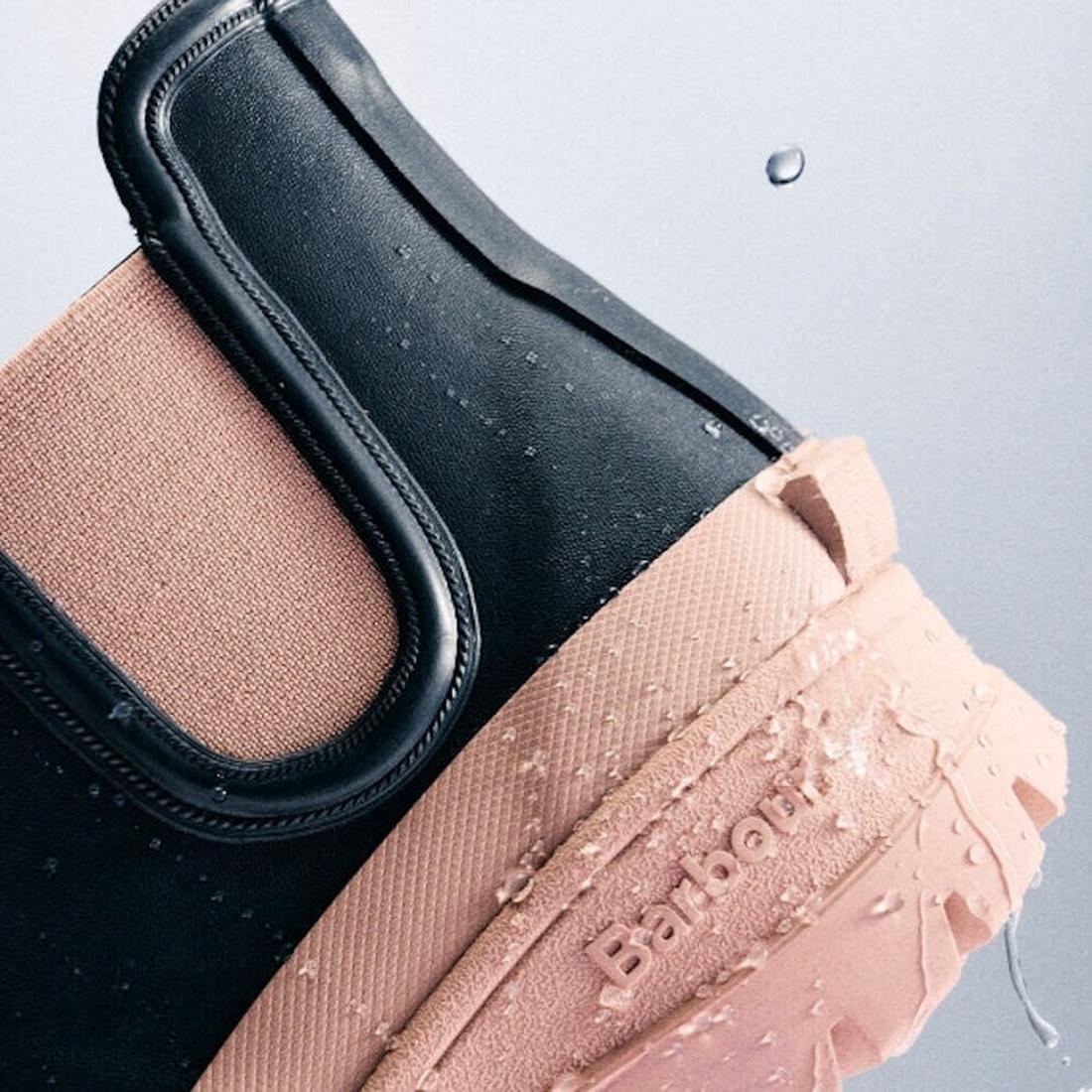 Close-up of Barbour Nimbus Dusky Grey/Gardenia Pink Chelsea Wellingtons—women’s rainboots with waterproof ankle design, black and pink color blocks, glistening water droplets, and Barbour embossed on the Gardenia Pink sole., 5063669171677, 5063669171684, 