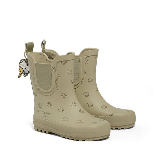 The Pretty Brave Puddle Boot Ankle Rainboot in Sage Green Smiley features smiley face patterns, a back pull tag, and a cloud and lightning bolt keychain. These waterproof kids’ boots blend playful style with practical design.