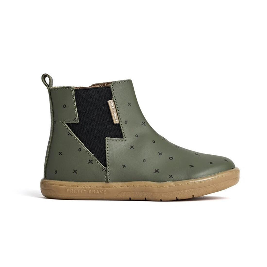 The Pretty Brave Electric Boot Khaki XO is a kids’ leather boot in olive green with a tan sole, black elastic side panel, small black X patterns, back pull tab, and a Pretty Brave label. The boot is shown from the side., 28805, 28806, 9420075305335, 94200