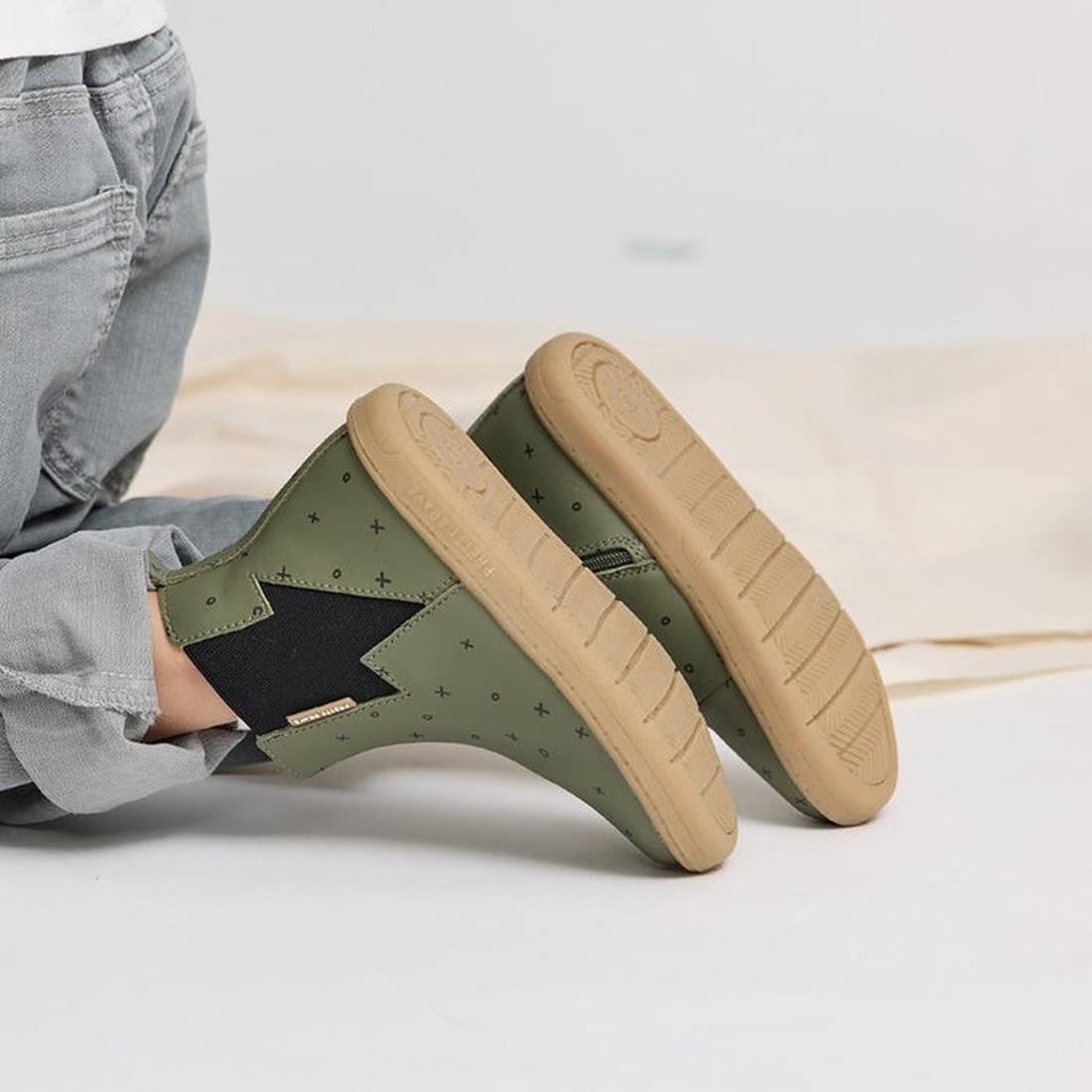 A child wearing light gray jeans and Pretty Brave Electric Boot Khaki XO boots with black lightning bolts and tan soles sits on a light surface with legs outstretched., 28805, 28806, 9420075305335, 9420075305342, 9420075305359, 9420075305366, 942007530537