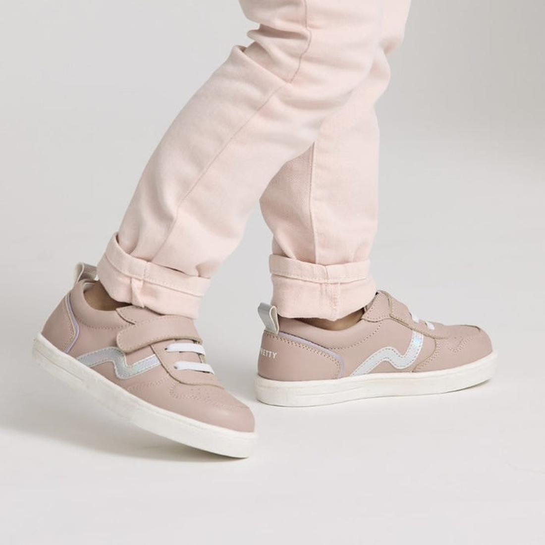 A child in light pink pants, shown from the knees down against a plain backdrop, steps forward wearing Pretty Brave XO Trainer Blush sneakers featuring blush pink with white soles and silver accents., 28764, 9420075304024, 9420075304031, 9420075304048, 94