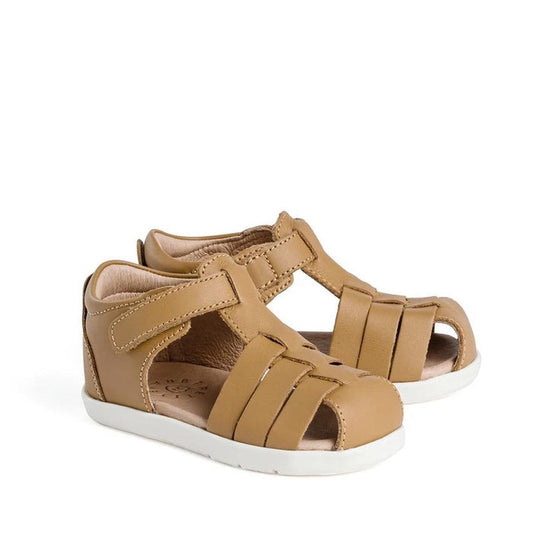 The Pretty Braver Billie First Walker Sandal Closed Back in tan is a children's early walker sandal with closed heels, open toes, white rubber soles, and adjustable hook-and-loop straps for a secure fit. Lightweight and flexible.