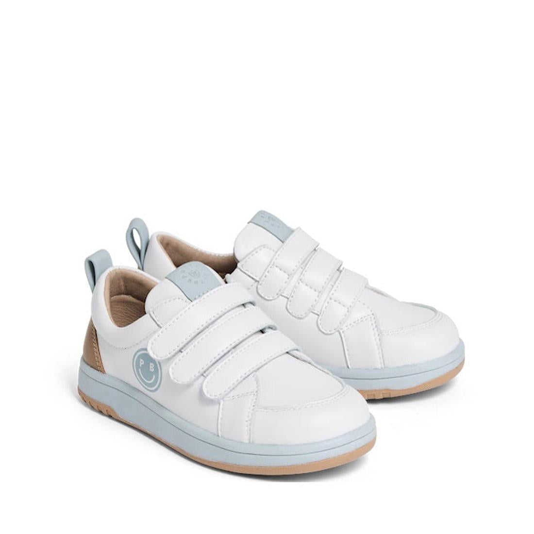 The Pretty Brave Happy Trainer White/Blue Sneaker is a kids’ genuine leather shoe with light blue accents, two Velcro straps, tan soles, and back pull tabs. Shown side by side on a plain white background.